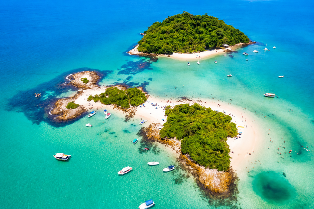 Vista aérea das ilhas paradisíacas de Angra dos Reis, Rio de Janeiro, com águas cristalinas, areia branca, vegetação preservada e barcos de passeio.