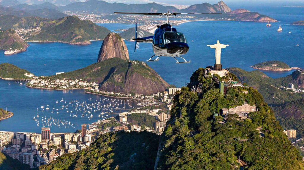 Vista aérea panorâmica do Rio de Janeiro com helicóptero sobrevoando o Cristo Redentor no Corcovado e o Pão de Açúcar na Baía de Guanabara.